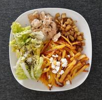 Homemade grilled chicken with french fries, grilled chopped eggplant and green salad, served on a white plate photo