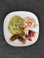 hecho en casa A la parrilla pollo con calabacín guiso, verde ensalada y Pepino pepinillos y jamón servido en un blanco plato foto