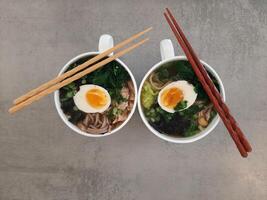 Asian ramen soba noodle soup close up with chicken, boiled egg, nori, green spinach and green onion served with chopsticks. Top view. photo