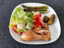 Homemade grilled chicken legs with grilled asparagus, green salad,  sliced tomatonand cucumber picklesy. photo