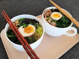 Asian ramen soba noodle soup close up with chicken, boiled egg, nori, green spinach and green onion served with chopsticks photo