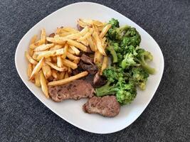 hecho en casa A la parrilla Cerdo con francés papas fritas y brócoli, servido en un blanco plato foto