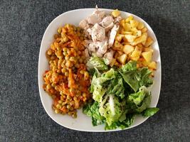 Homemade grilled chicken with french fries, green salad and pea stew served on a white plate photo