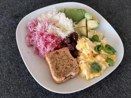 Homemade breakfast with avocado, scrambled eggs, olives, kohlrabi, reddish and a slice of bread served on a white plate photo