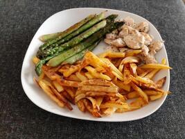 Homemade grilled chicken with french fries and grilled asparagus, served on a white plate photo