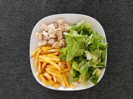 Homemade grilled chicken with french fries and green salad, served on a white plate photo