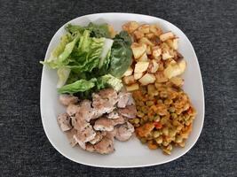 hecho en casa A la parrilla pollo con francés papas fritas, verde ensalada y guisante estofado servido en un blanco plato foto