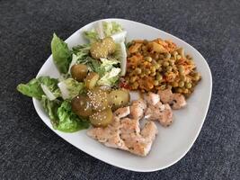 Homemade grilled chicken with green salad, peas stew and cucumber pickles served on a white plate photo