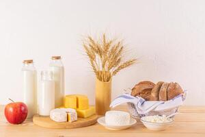 A variety of fresh dairy products, bread, ears of corn, apples on a wooden table. Treats and symbols of the Jewish holiday of Shavuot. photo