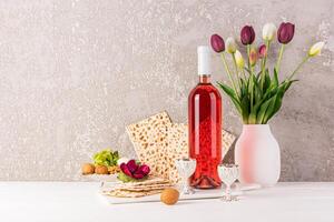 Still life for the Jewish Passover holiday. A bottle of kosher wine, freshly baked matzoth, walnuts, a vase of tulips on a light table. A copy space. photo