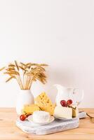 A beautiful still life for the holiday of Jewish Shavuot. Fresh dairy products, grapes and ears of bread on white vertical background photo