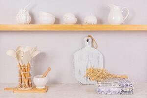 Bright kitchen space in a modern kitchen. Towels in a metal basket, a set of kitchen tools. Decorative pumpkins on an open wooden shelf. Front view. photo