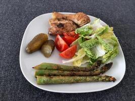 hecho en casa A la parrilla pollo piernas con A la parrilla espárragos, verde ensalada, rebanado tomatenand Pepino encurtido. foto