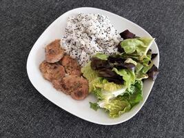 Homemade grilled pork with rice pilaf, and green salad, served on a white plate. Broccoli seeds on top of the rice pilaf photo