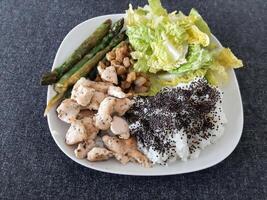 hecho en casa A la parrilla pollo con arroz, verde ensalada y A la parrilla espárragos, servido en un blanco lámina. brocolli semillas en parte superior de el arroz foto