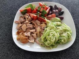 Homemade grilled chicken with zucchini, ovives, sliced tomato and basil leaves, served on a white plate photo