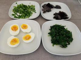 Homemade side dish with spinach, zucchini spirals, spring onions, boiled eggs and chopped nori algae served on white plates photo