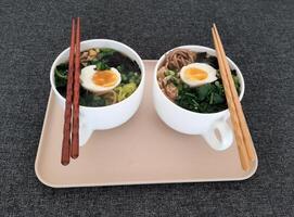 Asian ramen soba noodle soup close up with chicken, boiled egg, nori, green spinich and green onion served with chopsticks photo