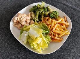 hecho en casa A la parrilla pollo con francés papas fritas, brócoli y verde ensalada, servido en un blanco plato foto