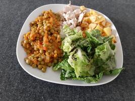 Homemade grilled chicken with french fries, green salad and pea stew served on a white plate photo