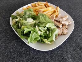 Homemade grilled chicken with french fries and green salad, served on a white plate photo