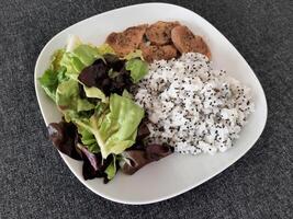 Homemade grilled pork with rice pilaf, and green salad, served on a white plate. Broccoli seeds on top of the rice pilaf photo