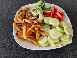 Homemade grilled chicken with french fries, cucumber, sliced tomato and green salad, served on a white plate photo