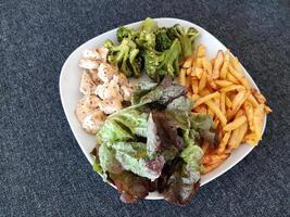 hecho en casa A la parrilla pollo con francés papas fritas, brócoli y verde ensalada, servido en un blanco plato foto