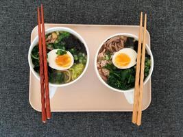 Asian ramen soba noodle soup close up with chicken, boiled egg, nori, green spinach and green onion served with chopsticks. Top view. photo