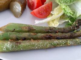 Homemade grilled chicken legs with grilled asparagus, green salad,  sliced tomatonand cucumber picklesy. photo