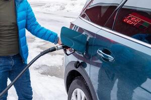 turista participación boquilla con repostaje petróleo en moderno suv coche durante el invierno viaje a yo Servicio gas estación foto