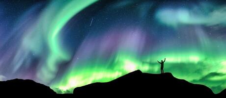 Aurora borealis glowing over silhouette hiker standing on the mountain in the night sky photo