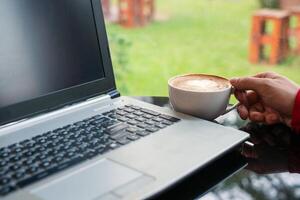 Hand of man holding hot coffee cup with modern laptop in cafe photo