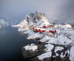 Red house fishing village with snow mountain in snowfall day photo