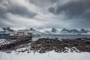 Snowy mountain range with stormy sky in fishing village on coastline in winter photo