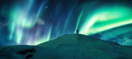 Aurora borealis glowing over silhouette hiker standing on the mountain in the night sky photo