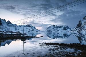 Snowy mountain range and electric pole reflection on coastline in rural area at Lofoten islands photo