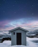 Wooden warehouse and colorful sky with stars on coastline in winter at Senja island photo