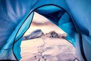 View from inside mountaineer tent of sunrise over snowy mountain peak on summit photo