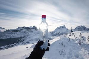 Hand of mountaineer holding water bottle on snow covered mountain in the morning photo