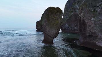 Aerial view of beautiful sea stack and dark cliffs in sunset. Calm seascape video