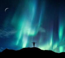 Aurora borealis glowing over silhouette hiker standing on the mountain in the night sky photo