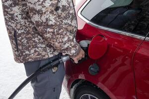 hombre participación combustible bomba boquilla con relleno bencina petróleo en rojo coche a autoservicio gasolina estación foto