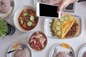 Variety of food with smartphone take a photo on dining table
