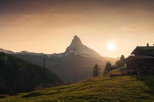 Sunset over Matterhorn mountain with wooden cottage on pasture in rural scene at Zermatt, Switzerland photo