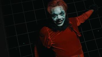 une homme dans une rouge costume et pitre maquillage des rires tandis que posant dans une très terrifiant pose, pendant Halloween video