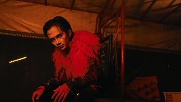 a man in creepy clown makeup poses in a haunted hut that glows red video