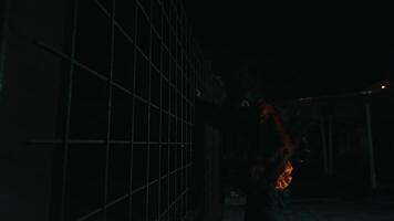 een Mens in een rood overhemd en clown bedenken dansen in voorkant van een ijzer hek terwijl poseren heel griezelig Bij nacht. video
