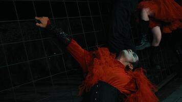 artístico retrato do uma pessoa com dramático Maquiagem deitado em uma lado a lado chão, vestindo uma vibrante vermelho pena boa. video