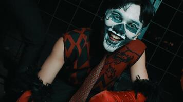 Person with skull face paint smiling in a dark, edgy setting with red and black attire. video